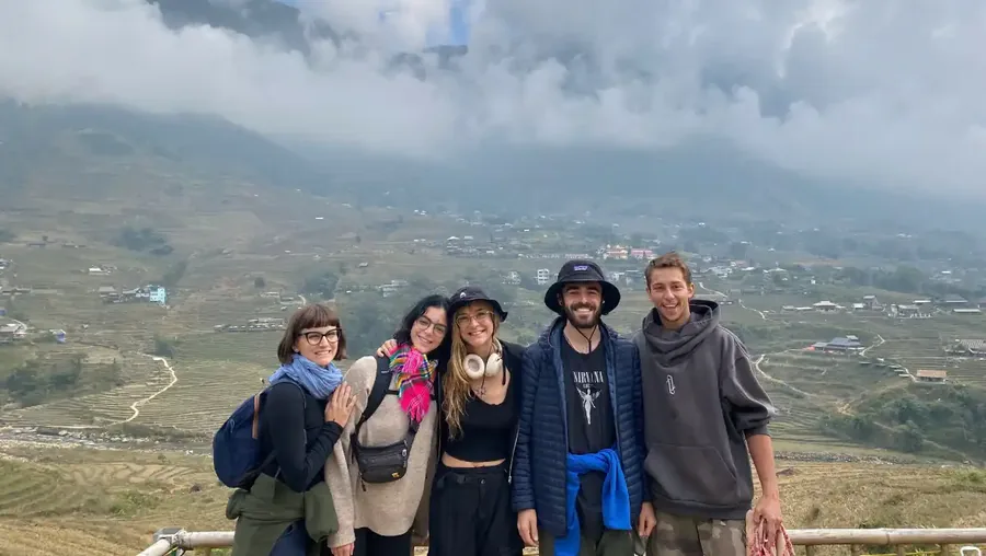 Group of travelers smiling together with Sapa rice terraces and misty mountains in the background