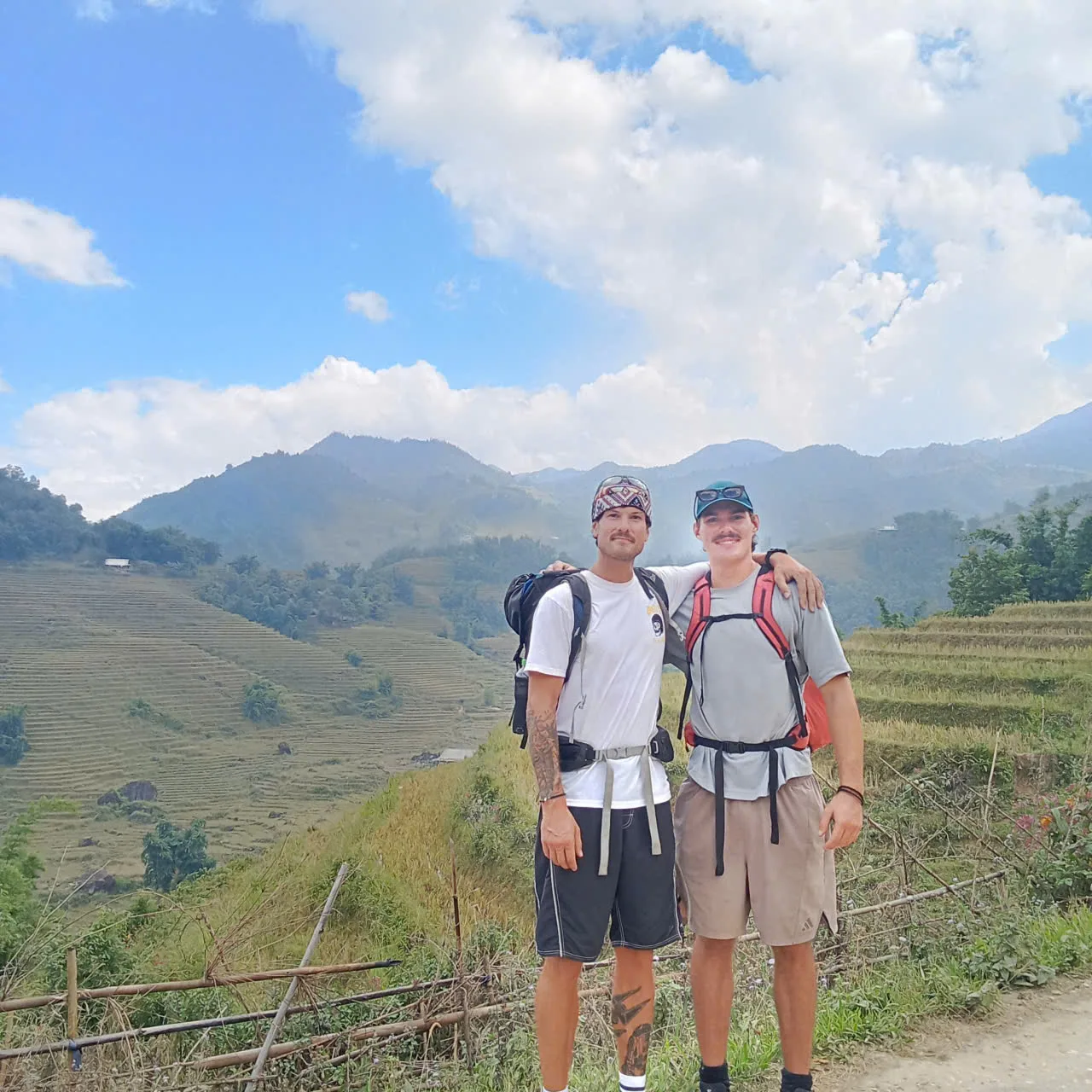 Two people with backpacks standing beside a wooden fence above rice terraces